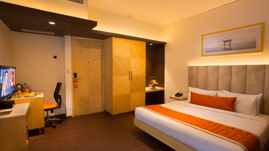 A comfortable Premium Room at Hotel Langford Keys by TGI with a double bed, padded headboard, side table with decor, wardrobe area, and a compact workspace.
