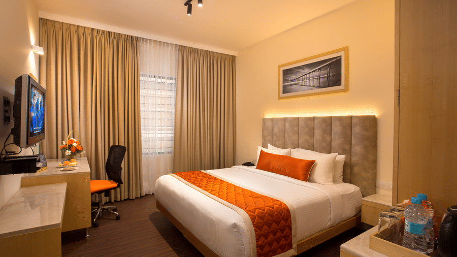A neatly arranged Premium Room at Hotel Langford Keys by TGI with a double bed, cushioned headboard, bedside lighting, a work desk with chair, and full-length window curtains.