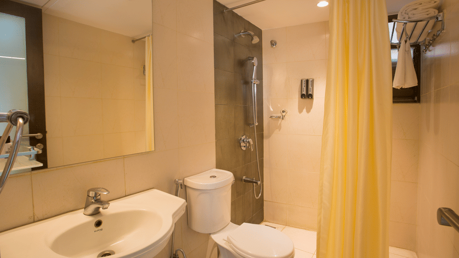 A compact bathroom of Premium Room at Hotel Langford Keys by TGI with a washbasin and mirror, a toilet, and a glass-enclosed shower area separated by a curtain.