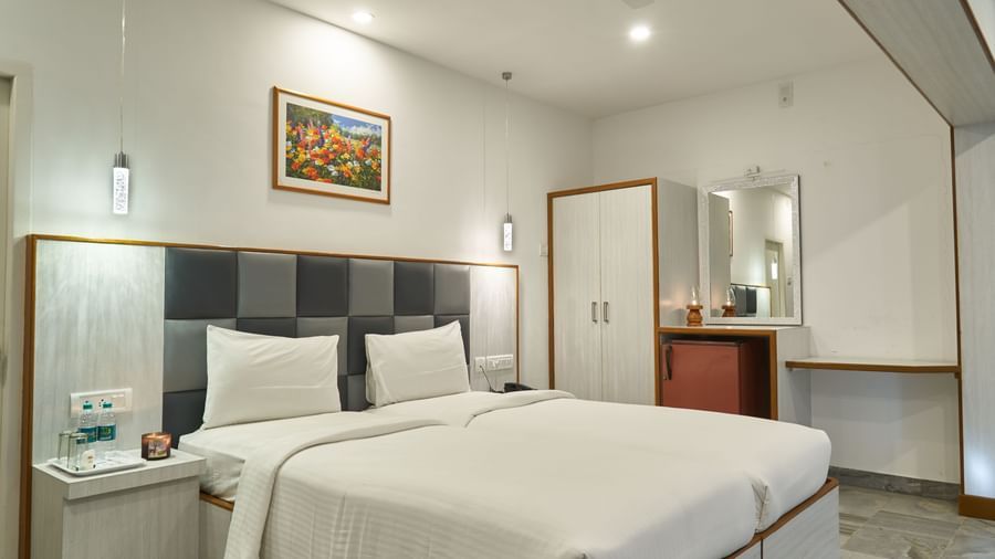 A comfortable and well-appointed hotel room at Hotel Mamallaa Heritage, featuring a large bed with crisp white linens, a bedside table, and wall-mounted art.