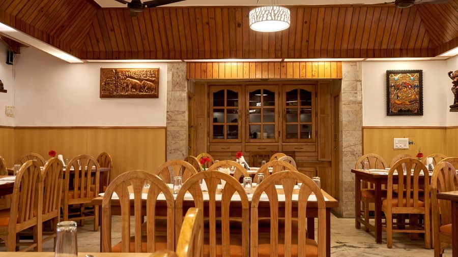 A perspective view within the restaurant at Hotel Mamallaa Heritage, showing an archway or passage leading to another section, with wooden furniture.