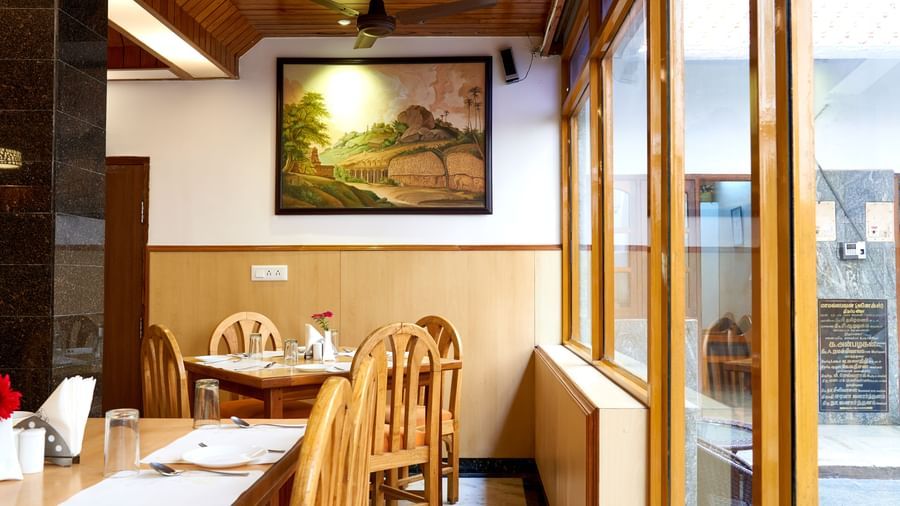A cosy section of the restaurant at Hotel Mamallaa Heritage, featuring wooden tables, chairs seating along the wall, with a painting on the wall.