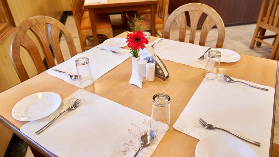 A close-up of a single dining table set with white plates, cutlery, glasses, and a small floral arrangement at Hotel Mamallaa Heritage's restaurant.