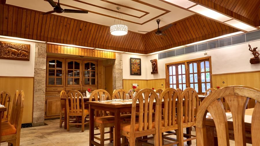 Another view of the restaurant at Hotel Mamallaa Heritage, showcasing multiple wooden dining sets and a distinctive patterned wooden ceiling.