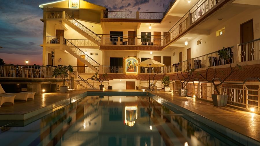 A nighttime view of Hotel Mamallaa Heritage, showcasing its illuminated facade and a beautifully lit swimming pool reflecting the lights.