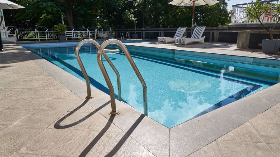 A close-up of the steps leading into the blue swimming pool at Hotel Mamallaa Heritage, with the poolside deck and lounge chairs visible.