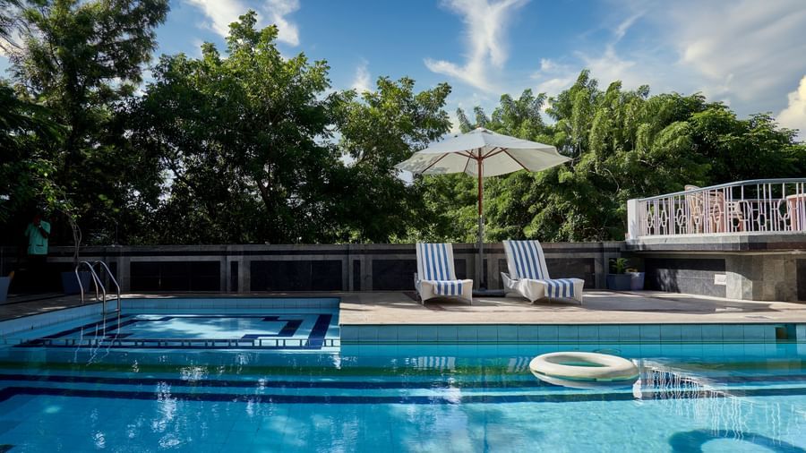 A serene view of the swimming pool at Hotel Mamallaa Heritage, surrounded by lush green trees and foliage, creating a relaxing atmosphere