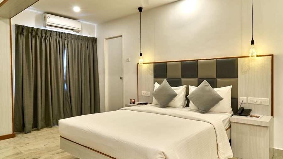 A clean and contemporary hotel room at Hotel Mamallaa Heritage, showcasing a bed with a light-coloured headboard, crisp white bedding, and modern lighting fixtures.