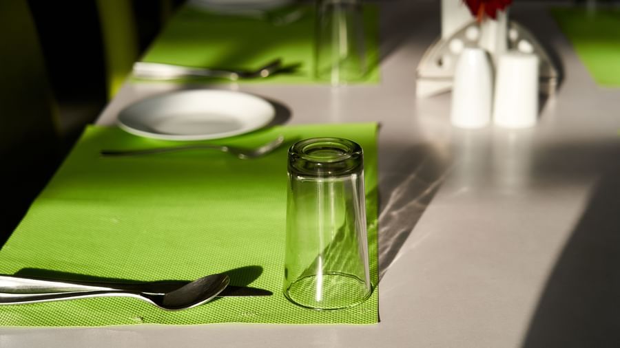 A detailed close-up of a table setting in the restaurant at Hotel Mamallaa Heritage, featuring a lime green placemat, white plate, and glassware.