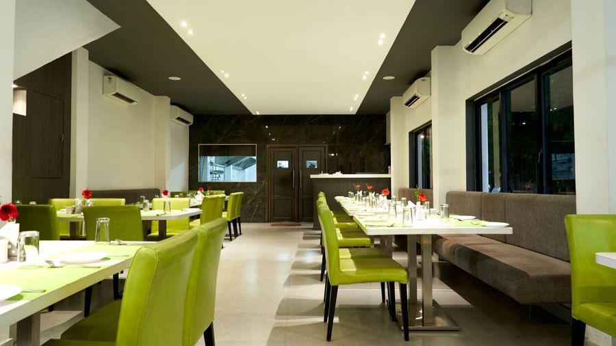 A modern restaurant interior at Hotel Mamallaa Heritage, characterized by bright lighting, white walls, and tables with vibrant lime green seating.