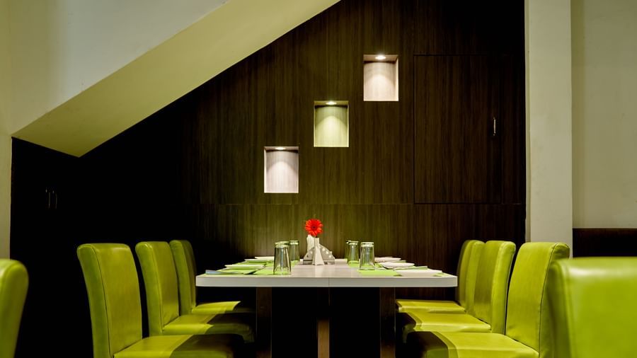 A dining table set with lime green chairs in the restaurant at Hotel Mamallaa Heritage, with stylish pendant lights hanging overhead.