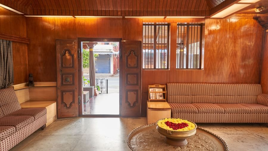 A warmly lit interior space at Hotel Mamallaa Heritage, showcasing a grand wooden doorway, traditional decor, and a low table with a decorative bowl.