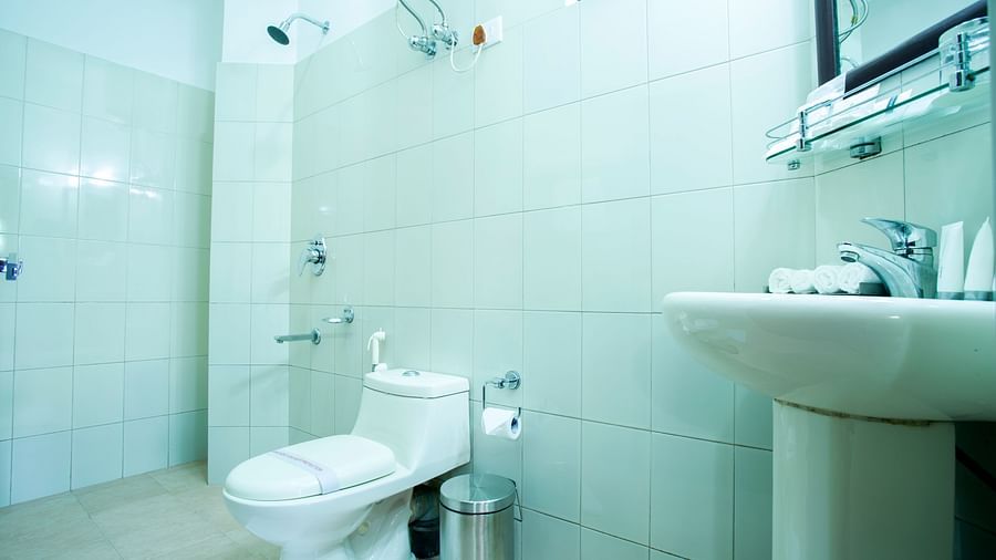 A bathroom at New Orchid Lords Inn Gangtok contains a toilet, a sink with a mirror and toiletries, and a shower area with shower heads.