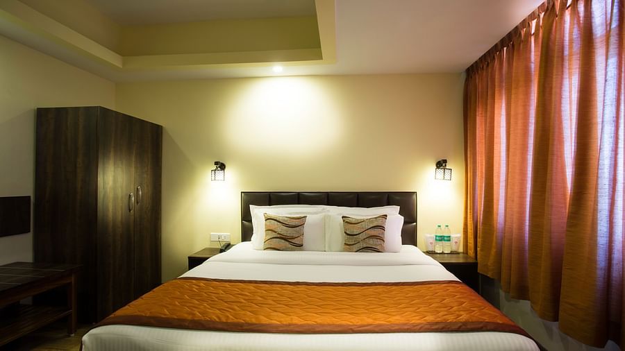 A room at New Orchid Lords Inn Gangtok contains a bed with pillows, bedside tables with lamps and water, curtains, and a wardrobe.
