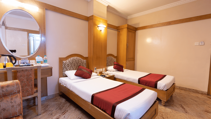 Twin-bedded room with wooden furniture and a vanity mirror at Hotel Pai Comforts, JP Nagar.