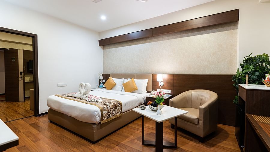 a double bed with a single seater sofa and a table next to it inside one of the rooms - Hotel Pai Vista, Mysore