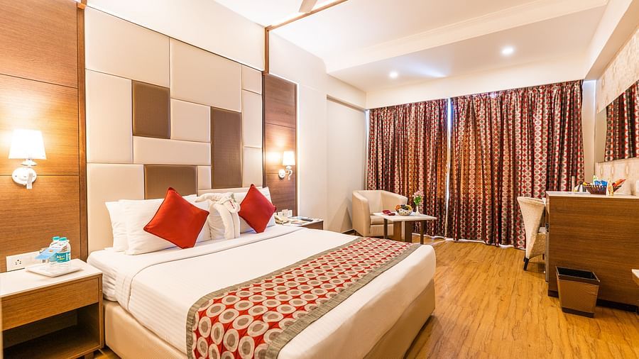 a double bed with side tables, lamps and sofa next to it inside one of the rooms - Hotel Pai Vista, Mysore