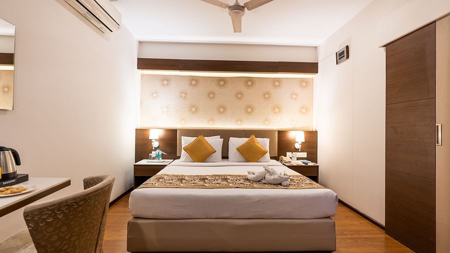 a double bed with a fan hung above it and an AC next to it inside one of the rooms - Hotel Pai Vista, Mysore