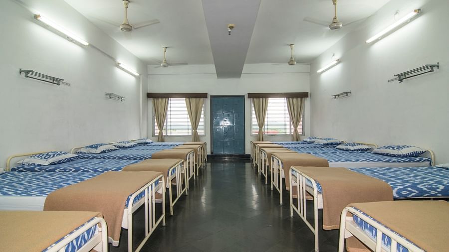 A full view of beds with bedding arranged in two rows in a room at Hotel Sahara - Spacious Dormitory in Ramoji Film City, Hyderabad.