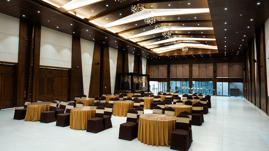 A large indoor event space featuring a dark wooden ceiling, round tables and brown chairs at Hotel Sonar Bangla, Ajodhya Hills.