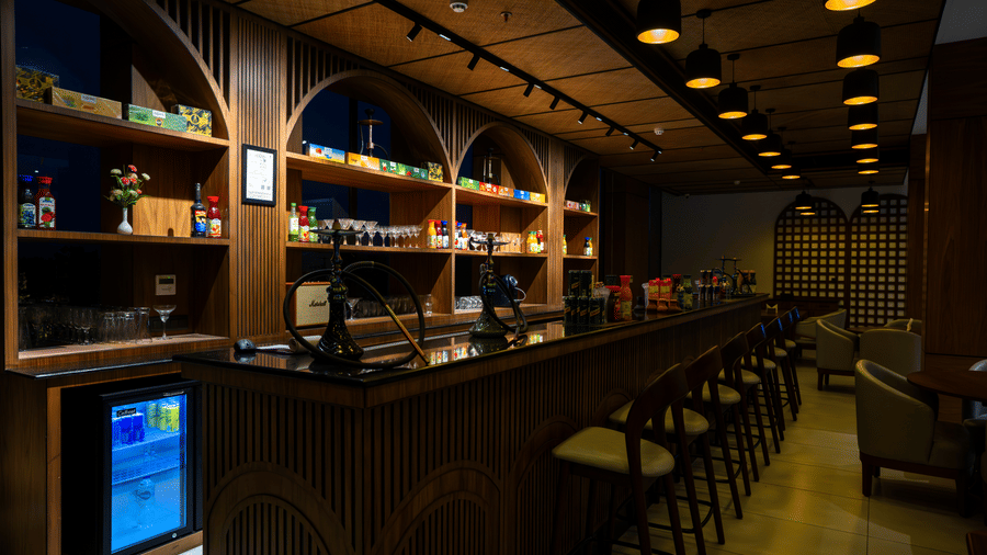 A wooden bar counter featuring tall stools and illuminated arched shelving at Hotel Sonar Bangla, Ajodhya Hills.