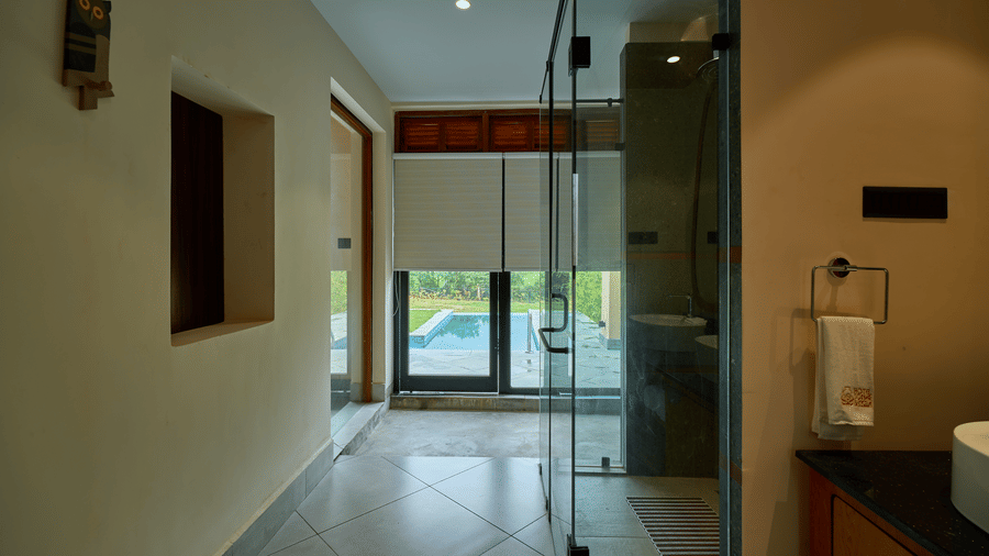 A tiled corridor featuring glass shower doors and a view leading towards an outdoor swimming pool at Hotel Sonar Bangla, Ajodhya Hills.