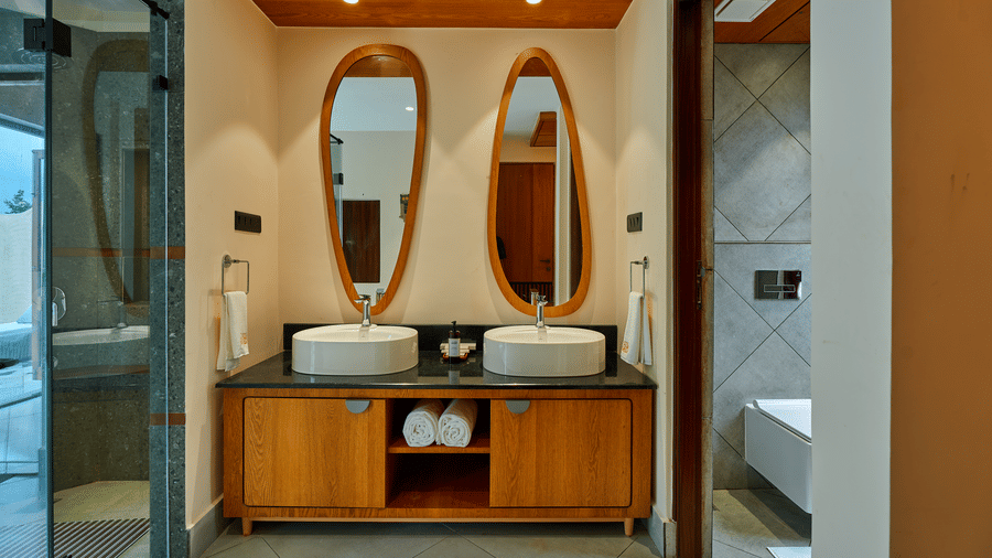 A bathroom featuring a wooden vanity unit with double white sinks and 2 oval mirrors at Hotel Sonar Bangla, Ajodhya Hills.