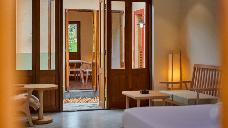 A bedroom interior featuring wooden furniture and open folding doors leading to another room at Hotel Sonar Bangla, Ajodhya Hills.