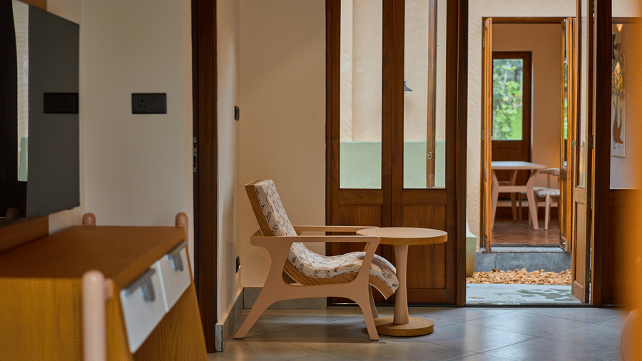 A bedroom featuring a wooden chair, a television on a stand, and open folding doors at Hotel Sonar Bangla, Ajodhya Hills.