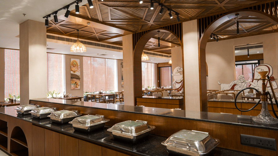 A dining area featuring a long counter with covered metal buffet dishes at Hotel Sonar Bangla, Ajodhya Hills.