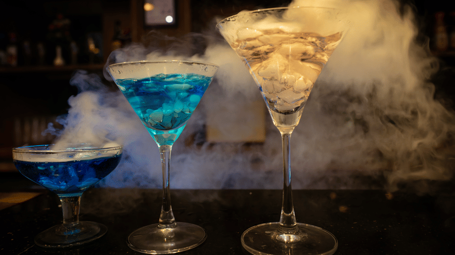 3 cocktail glasses featuring blue and clear drinks surrounded by thick smoke at Hotel Sonar Bangla, Ajodhya Hills.