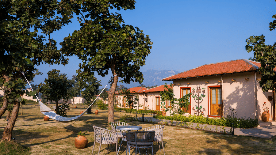 An outdoor area featuring a white hammock, patio seating, and a light-coloured cottage with a terracotta roof at Hotel Sonar Bangla, Ajodhya Hills.