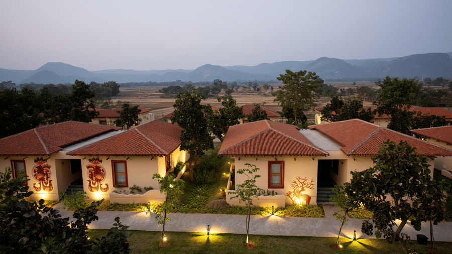 An elevated evening view featuring a row of cottages with warm lighting, pathways, and distant hills at Hotel Sonar Bangla, Ajodhya Hills.