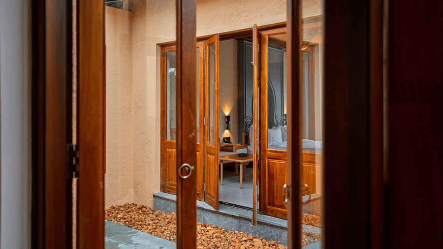 A view through wooden doors featuring an open courtyard with gravel leading to another open room at Hotel Sonar Bangla, Ajodhya Hills.
