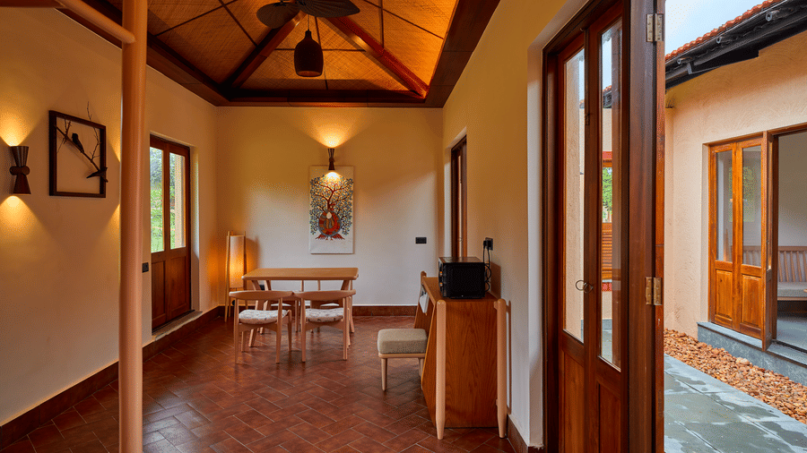 A living area featuring a dining table with chairs, terracotta flooring, and open wooden doors at Hotel Sonar Bangla, Ajodhya Hills.