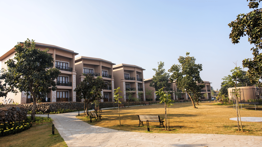 A wide exterior view featuring a paved path, lawns, trees, and multi-storey buildings with balconies at Hotel Sonar Bangla, Ajodhya Hills.