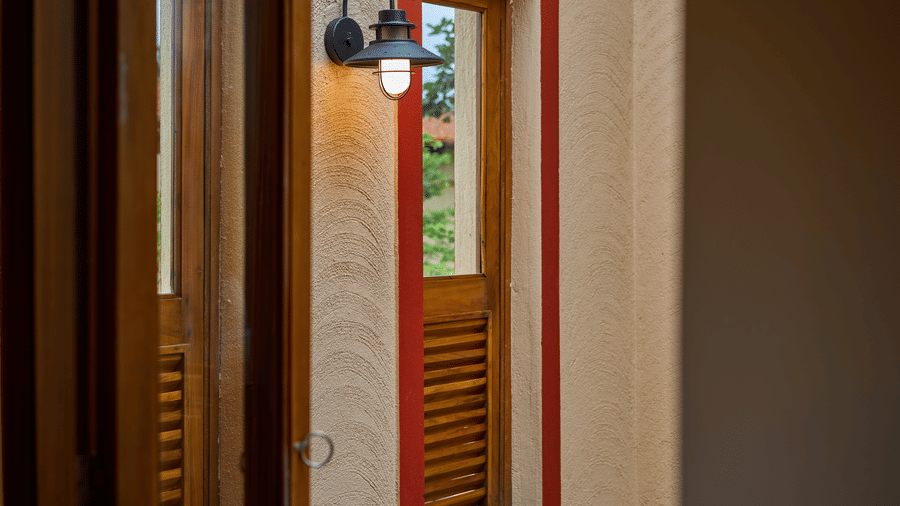 An exterior wall featuring a slatted wooden window, red trim, and an outdoor wall lamp at Hotel Sonar Bangla, Ajodhya Hills.