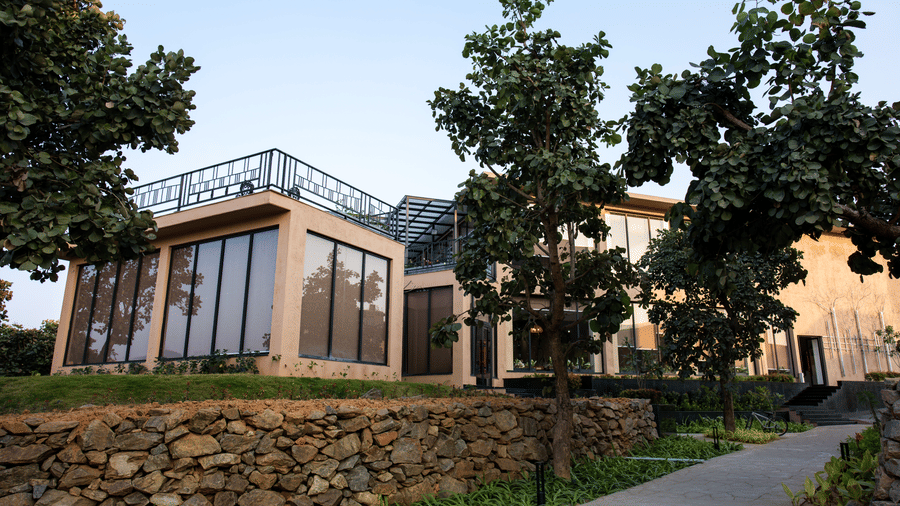 A building exterior featuring large windows, a paved path, and a stone wall at Hotel Sonar Bangla, Ajodhya Hills.