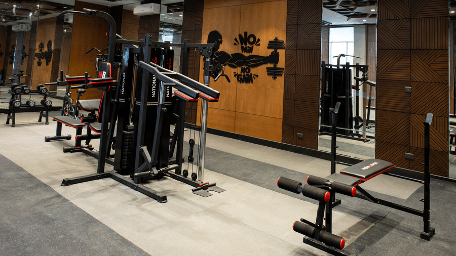 An indoor fitness centre featuring black workout machines, a weight bench, and mirrored walls at Hotel Sonar Bangla, Ajodhya Hills.