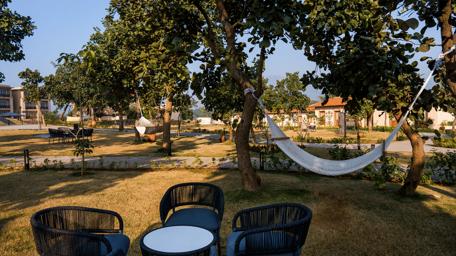 An outdoor area featuring a white hammock strung between trees and chairs around a table at Hotel Sonar Bangla, Ajodhya Hills.