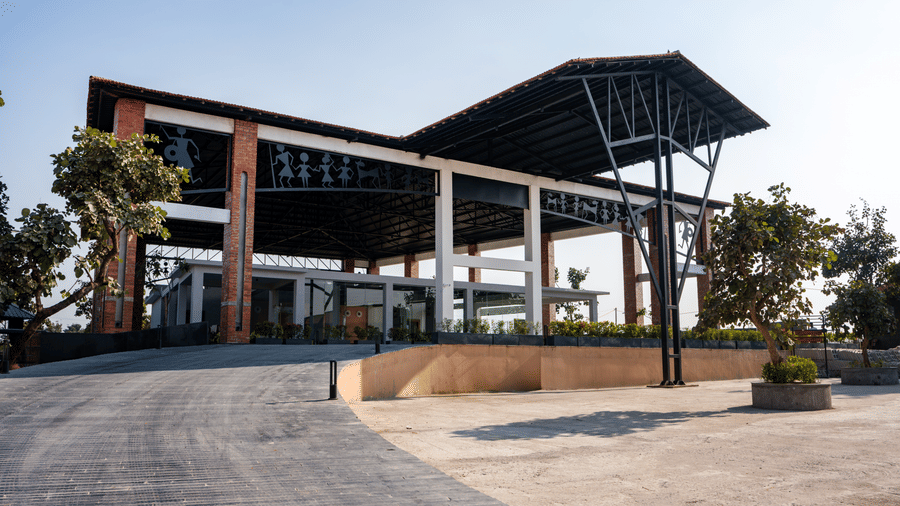 An exterior view featuring a modern building with a large dark angular canopy, tall brick pillars, and a paved driveway leading to the entrance at Hotel Sonar Bangla, Ajodhya Hills.