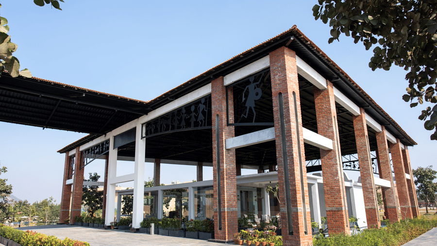 An angled exterior view featuring a modern building with thick brick pillars supporting a high dark roof over a paved entrance area at Hotel Sonar Bangla, Ajodhya Hills.
