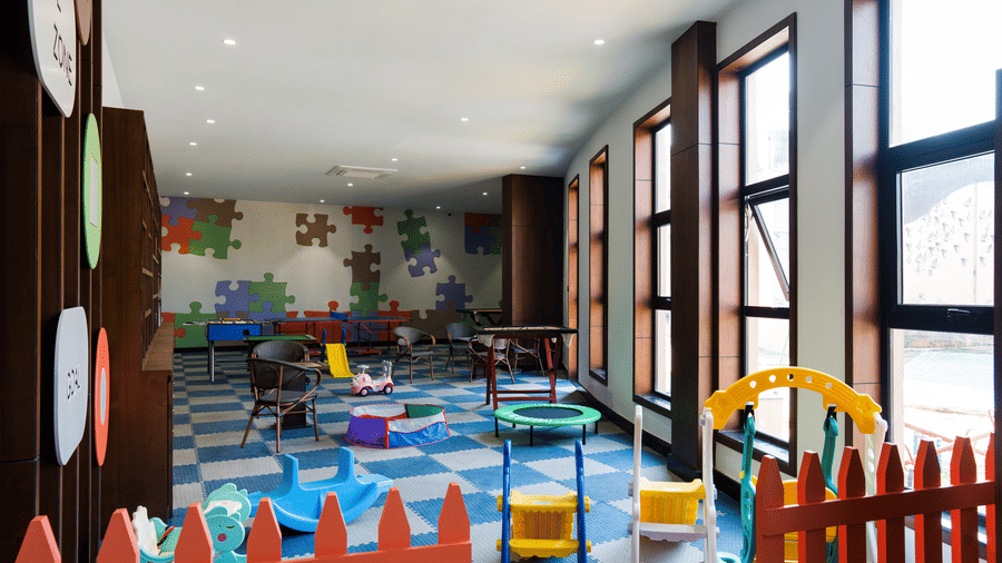 An indoor playroom featuring large windows, a checkered floor, and colourful children's play equipment at Hotel Sonar Bangla, Ajodhya Hills.