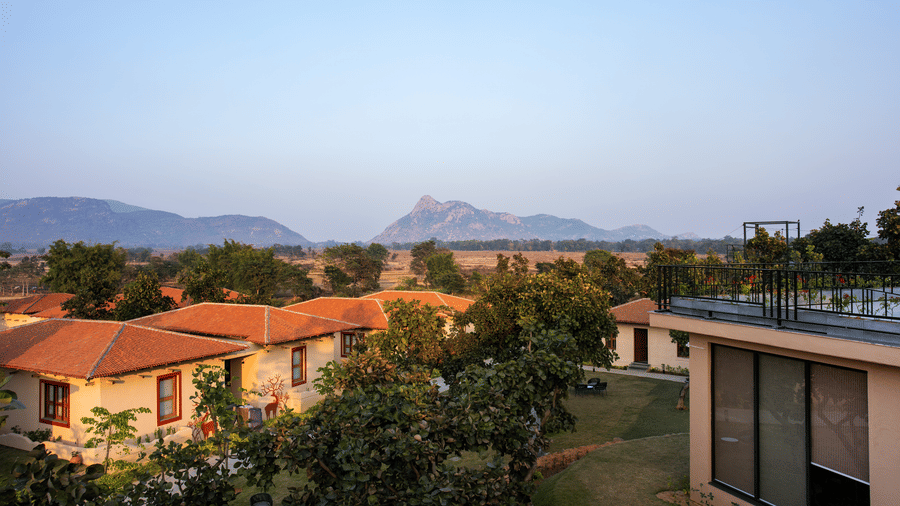 Buildings with terracotta roofs amongst trees with a hill behind at Hotel Sonar Bangla, Ajodhya Hills.