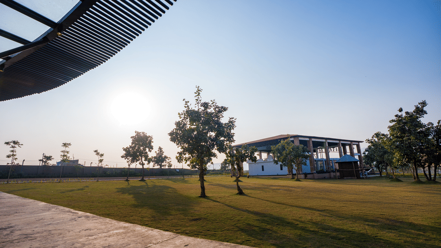 A large grassy outdoor area featuring scattered trees and a building in the distance under a clear sky at Hotel Sonar Bangla, Ajodhya Hills.