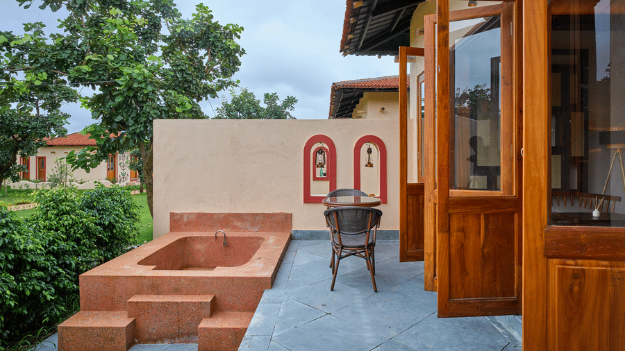 An outdoor patio featuring a stone bathtub, open wooden doors, and green plants at Hotel Sonar Bangla, Ajodhya Hills.