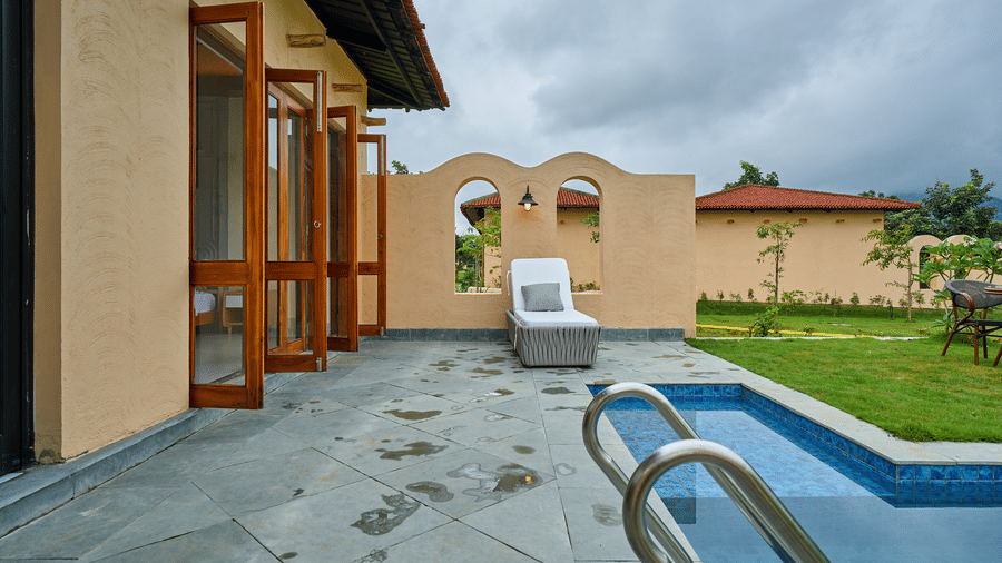 An outdoor patio featuring a swimming pool, a lounge chair, and open wooden doors at Hotel Sonar Bangla, Ajodhya Hills.