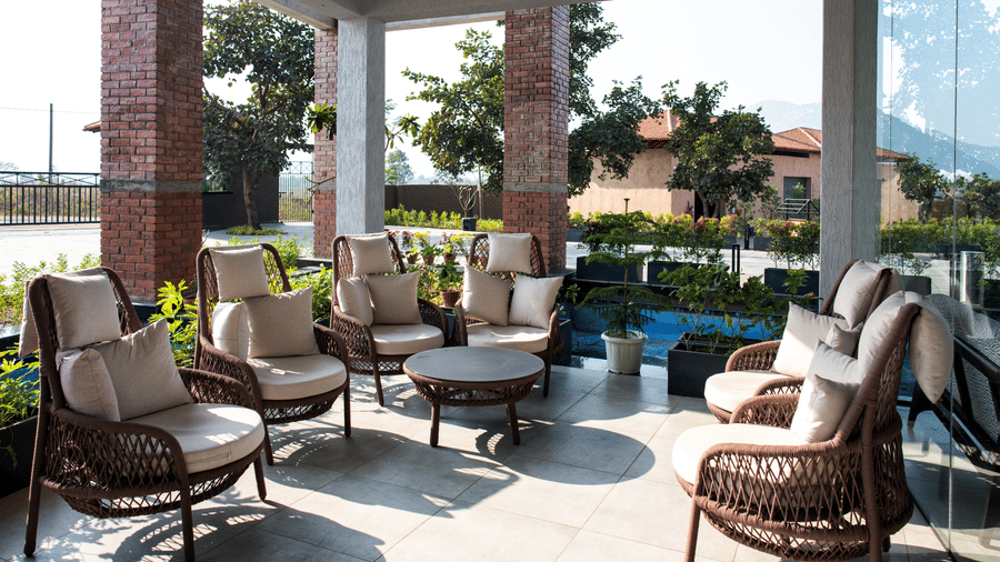 A covered patio featuring woven armchairs with white cushions arranged around a table at Hotel Sonar Bangla, Ajodhya Hills.