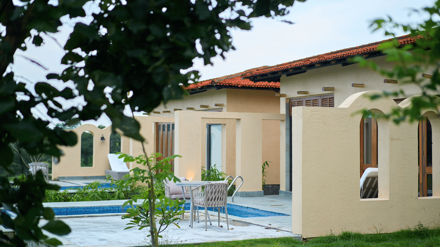 An outdoor area featuring a swimming pool, a lawn, patio seating, single storey buildings with terracotta roofs at Hotel Sonar Bangla, Ajodhya Hills.