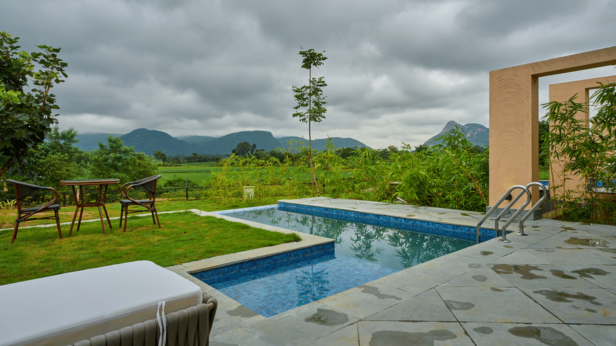 An outdoor area featuring an L-shaped swimming pool, a green lawn, patio seating, and distant hills at Hotel Sonar Bangla, Ajodhya Hills.